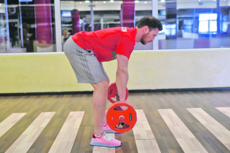 VEŽBA 2 (VESLANJE U PRETKLONU) - korak 1 - Dobra je za mišiće donjeg dela leđa. Počinjemo u položaju gde smo u pretklonu. Kolena su blago savijena, stopala su u širini ramena. Stomak je uvučen, kolena su fiksirana, malo povijena. Gornji deo tela je u pretklonu i trudimo se da bude što horizontalniji.