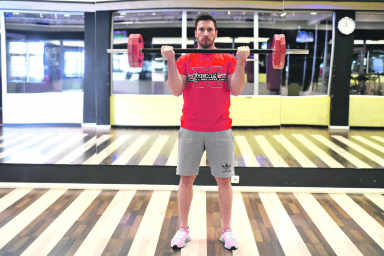 VEŽBA 4 - korak 2 - Fleksijom u zglobu lakta angažujemo biceps i privlačimo ruke skroz gore do brade, tj. grudi. Stopala su u širini ramena, telo je pravo. Postoje dve varijante ove vežbe. Može da se radi podizanjem opterećenja dopola ili celom dužinom, što je daleko bolje i efikasnije.