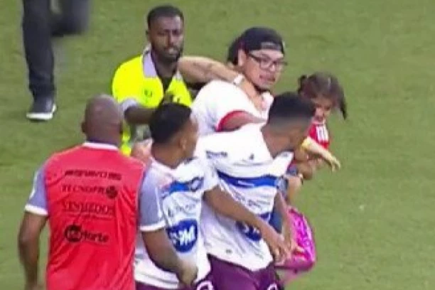 LUDILO EPSKIH RAZMERA! Huligan sa DETETOM U NARUČJU utrčao na teren i NAPAO fudbalera! (VIDEO)