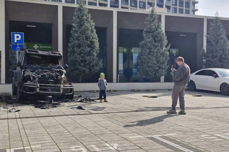 Ljudi se fotkaju ispred zapaljenog automobila